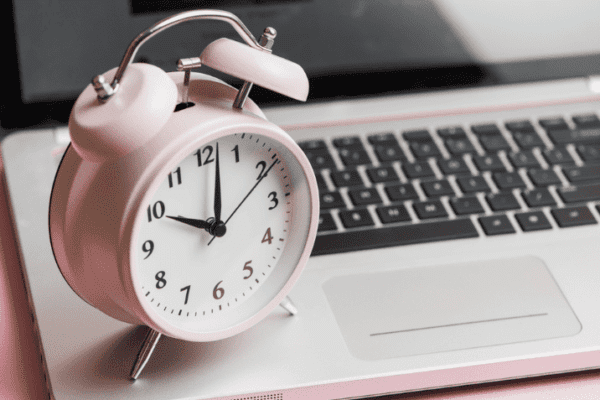 Pink alarm clock next to a laptop representing time management tips