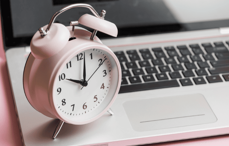 Pink alarm clock next to a laptop representing time management tips