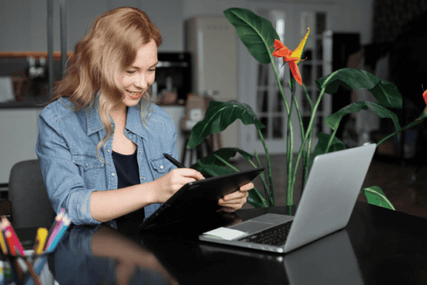 A person enhancing remote work productivity by using a digital tablet and stylus in front of a laptop.