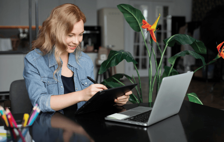 A person enhancing remote work productivity by using a digital tablet and stylus in front of a laptop.