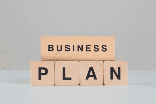 Wooden blocks spelling “BUSINESS PLAN” with text below showing key elements of business plan essentials