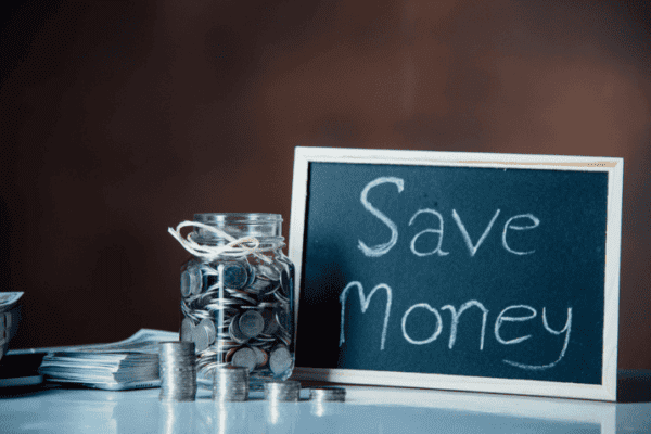 Glass jar filled with coins and a chalkboard with ‘Save Money’ representing startup marketing strategies for low budget