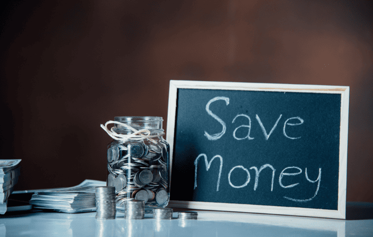 Glass jar filled with coins and a chalkboard with ‘Save Money’ representing startup marketing strategies for low budget