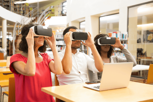 Three individuals using laptops in a library, discussing AR VR trends in education