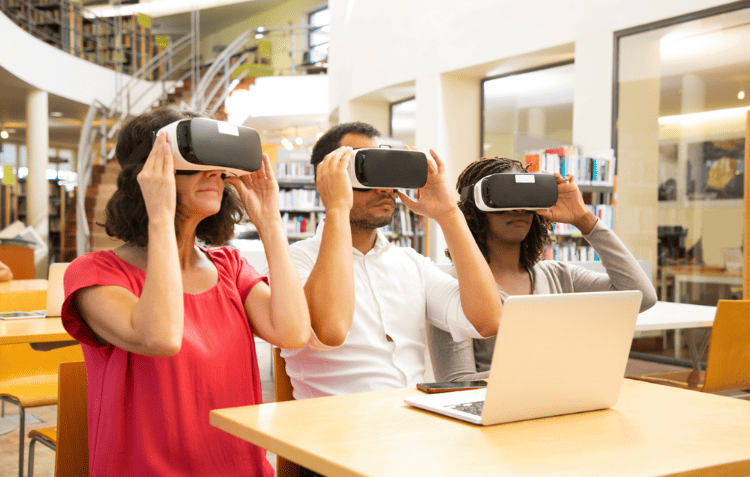 Three individuals using laptops in a library, discussing AR VR trends in education