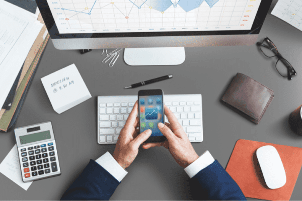 Desk with a smartphone, calculator, notebook, and papers with graphs and charts representing productivity tools in 2024.