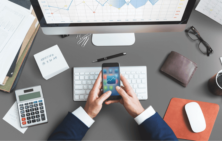 Desk with a smartphone, calculator, notebook, and papers with graphs and charts representing productivity tools in 2024.