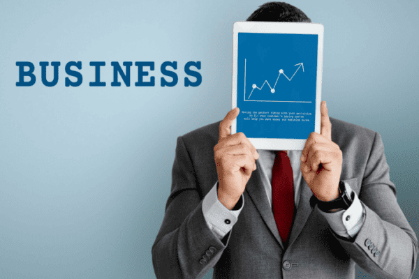 Person holding a blue book titled “BUSINESS” with a white upward trending graph showing to business scaling tips