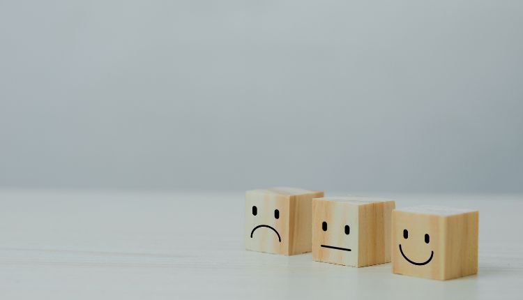 Wooden blocks with sad, neutral, and happy faces representing customer feedback.